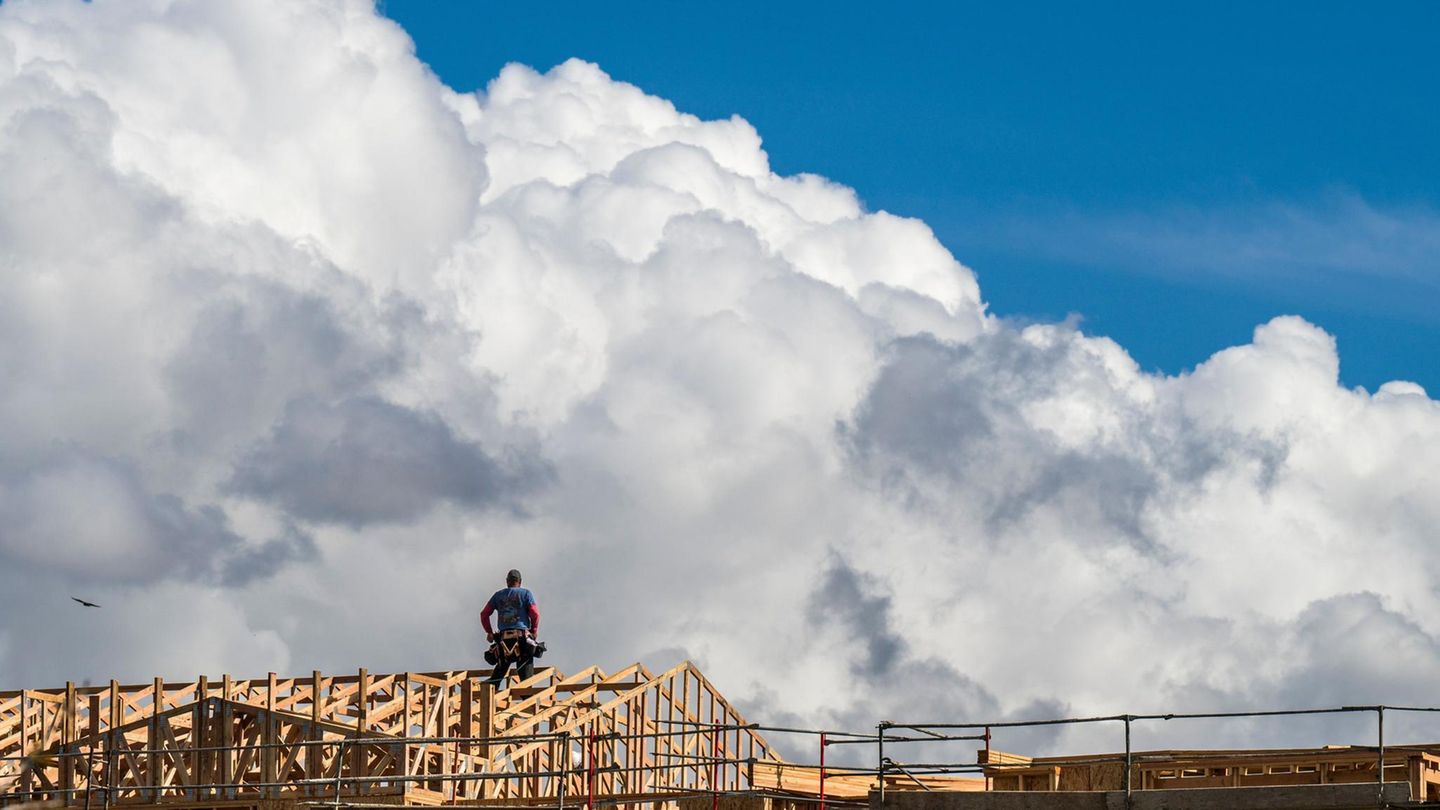 Ein Bauarbeiter macht eine Verschnaufpause, während sich Wolken über einem Hausbauprojekt auftürmen