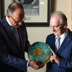 Merz nimmt eine Nachbildung der Himmelsscheibe von Nebra entgegen. Foto: Robert Michael/dpa