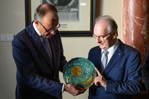 Merz nimmt eine Nachbildung der Himmelsscheibe von Nebra entgegen. Foto: Robert Michael/dpa