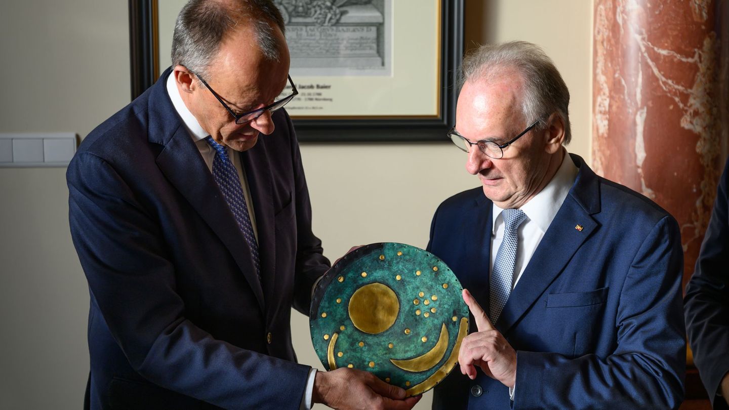 Merz nimmt eine Nachbildung der Himmelsscheibe von Nebra entgegen. Foto: Robert Michael/dpa