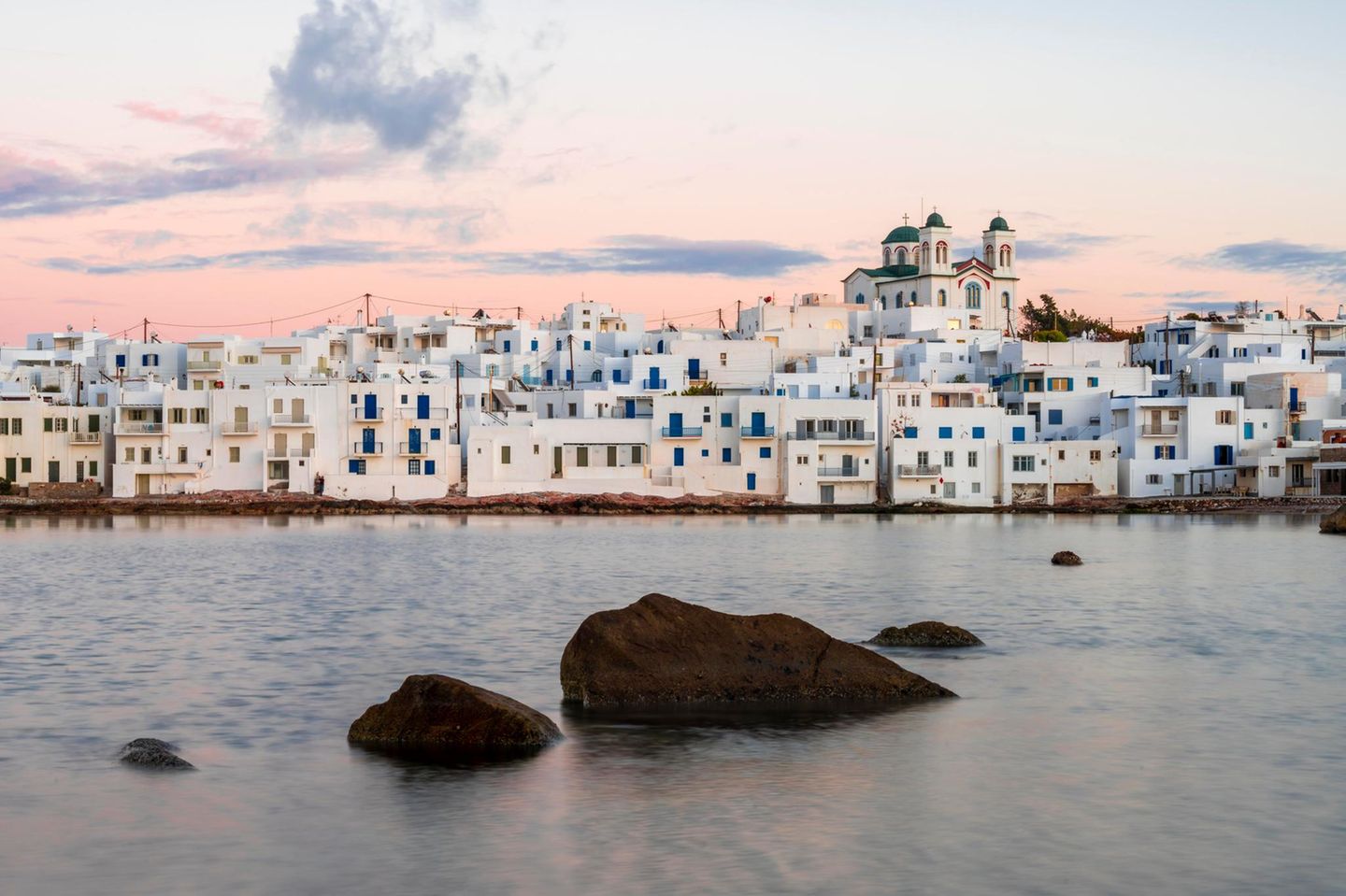 Weiße Häuser am Wasser in Paros, der Himmel in rosa-Tönen