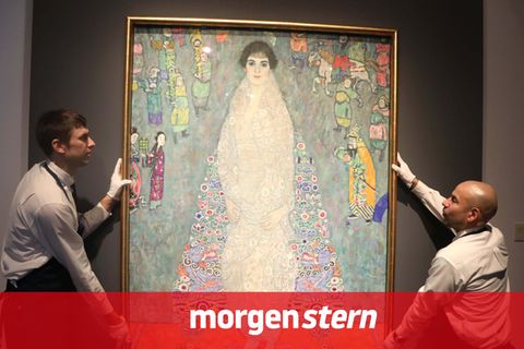 Zwei Mitarbeiter hängen ein Gemälde von Gustav Klimt auf