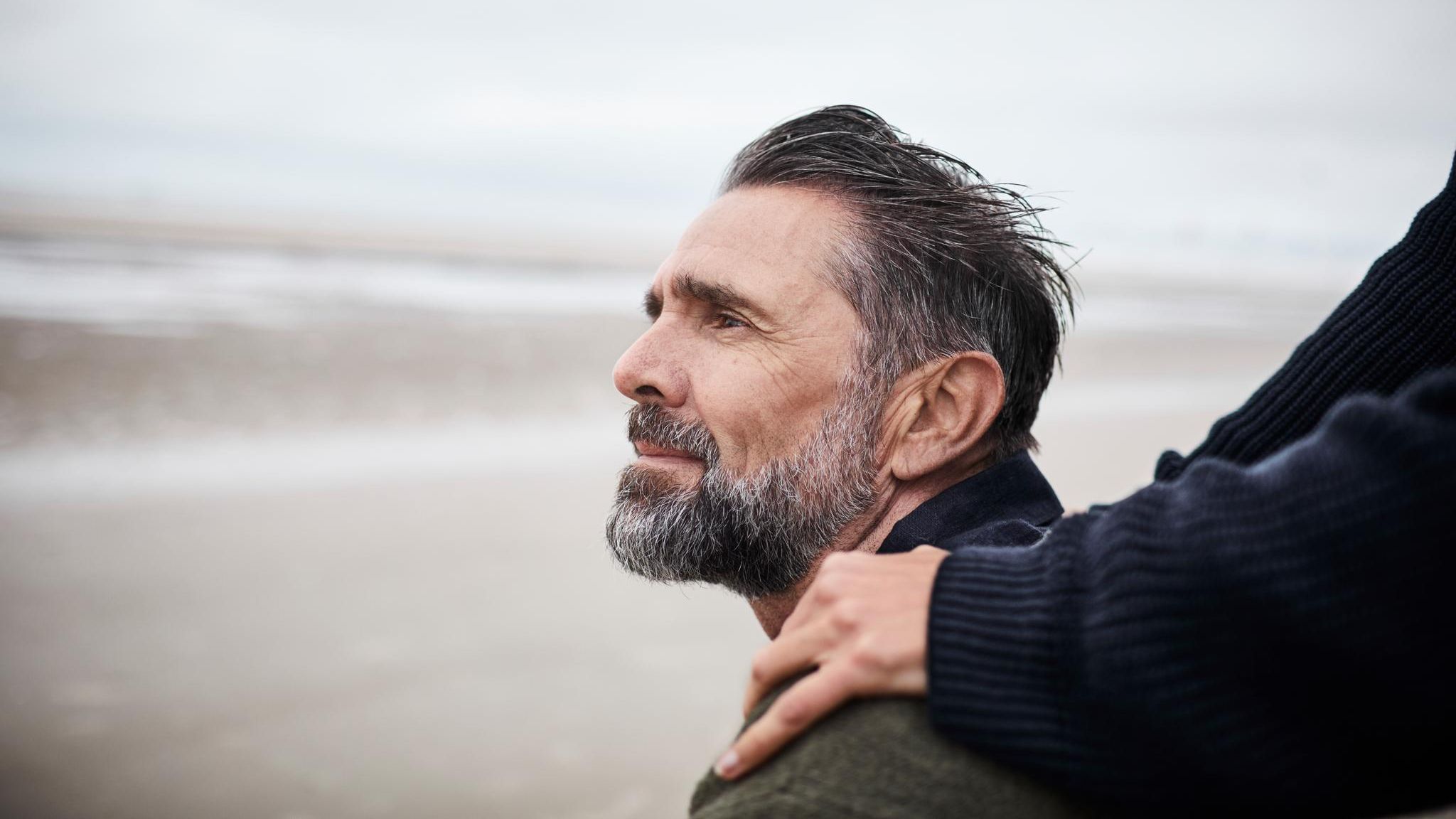 Ein Mann am Strand mit den Händen einer Frau auf seinen Schultern