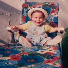 Symbolbild Kindheitserinnerungen: Kleinkind in den 90ern sitzt auf einem geblümten Gartenstuhl