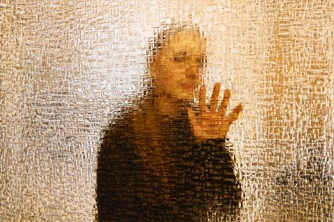 Hinter einer Glaswand erkennt man unscharf eine weibliche Gestalt. Hadert sie mit ihrewr identität?