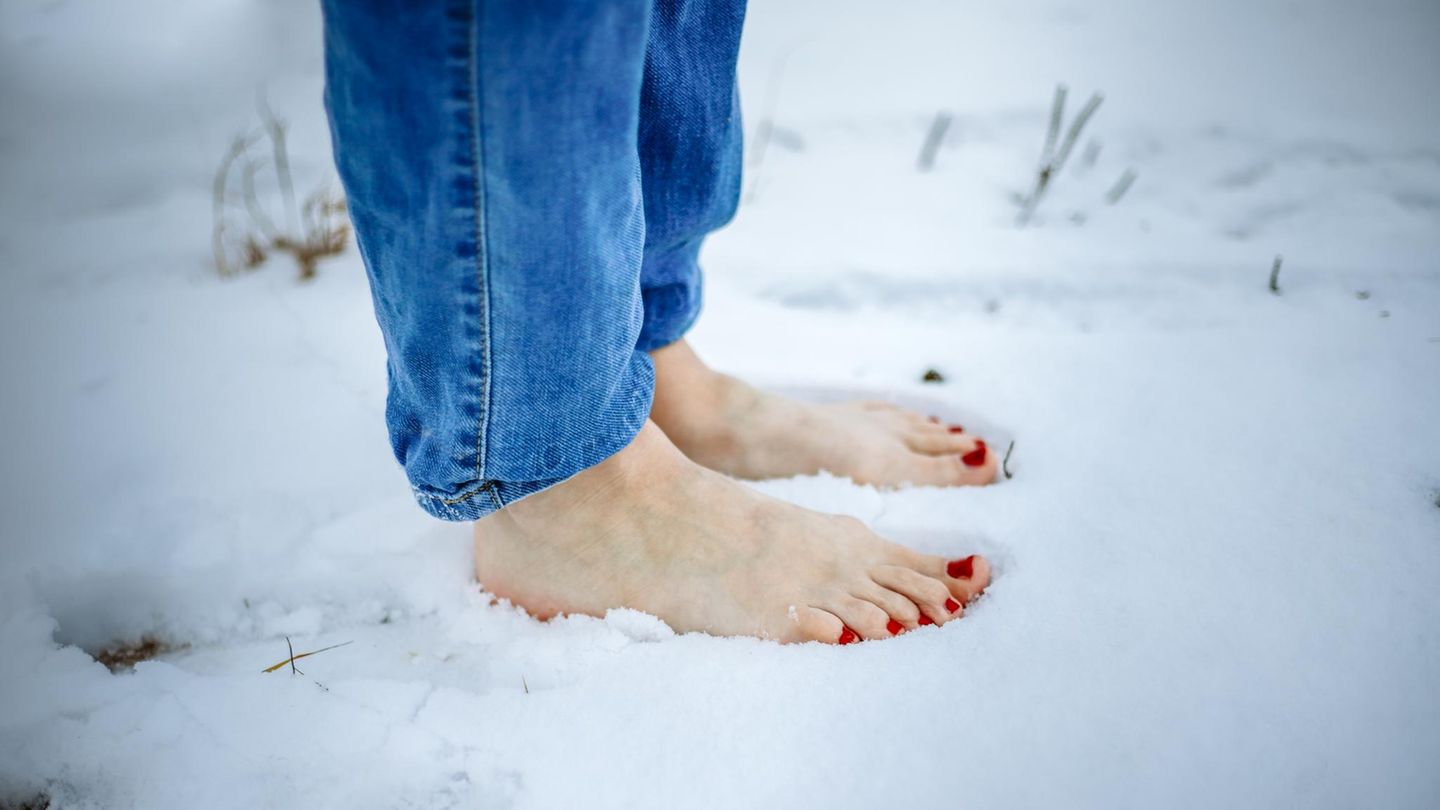 Erkältung durch kalte Füße: Frau steht barfuß im Schnee