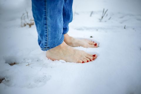 Erkältung durch kalte Füße: Frau steht barfuß im Schnee