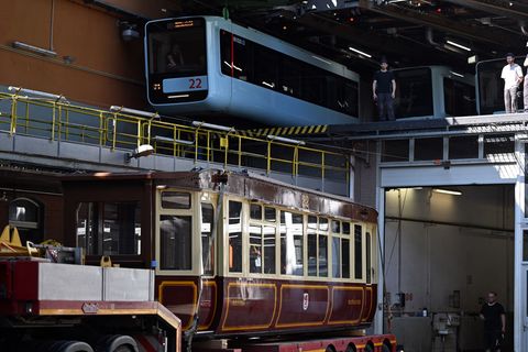 Die Schwebebahn gestern und heute. Ein Wagen der ersten Baureihe 1900 steht auf einem Tieflader unter einem Wagen der aktuellen