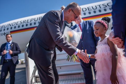 Kanzler Friedrich Merz wird auf dem Flughafen von Johannesburg von einem Mädchen begrüßt. Foto: Michael Kappeler/dpa