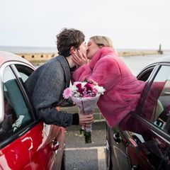 Date: Zwei Menschen lehnen sich aus den Fenstern nebeneinanderstehender Autos und küssen sich.