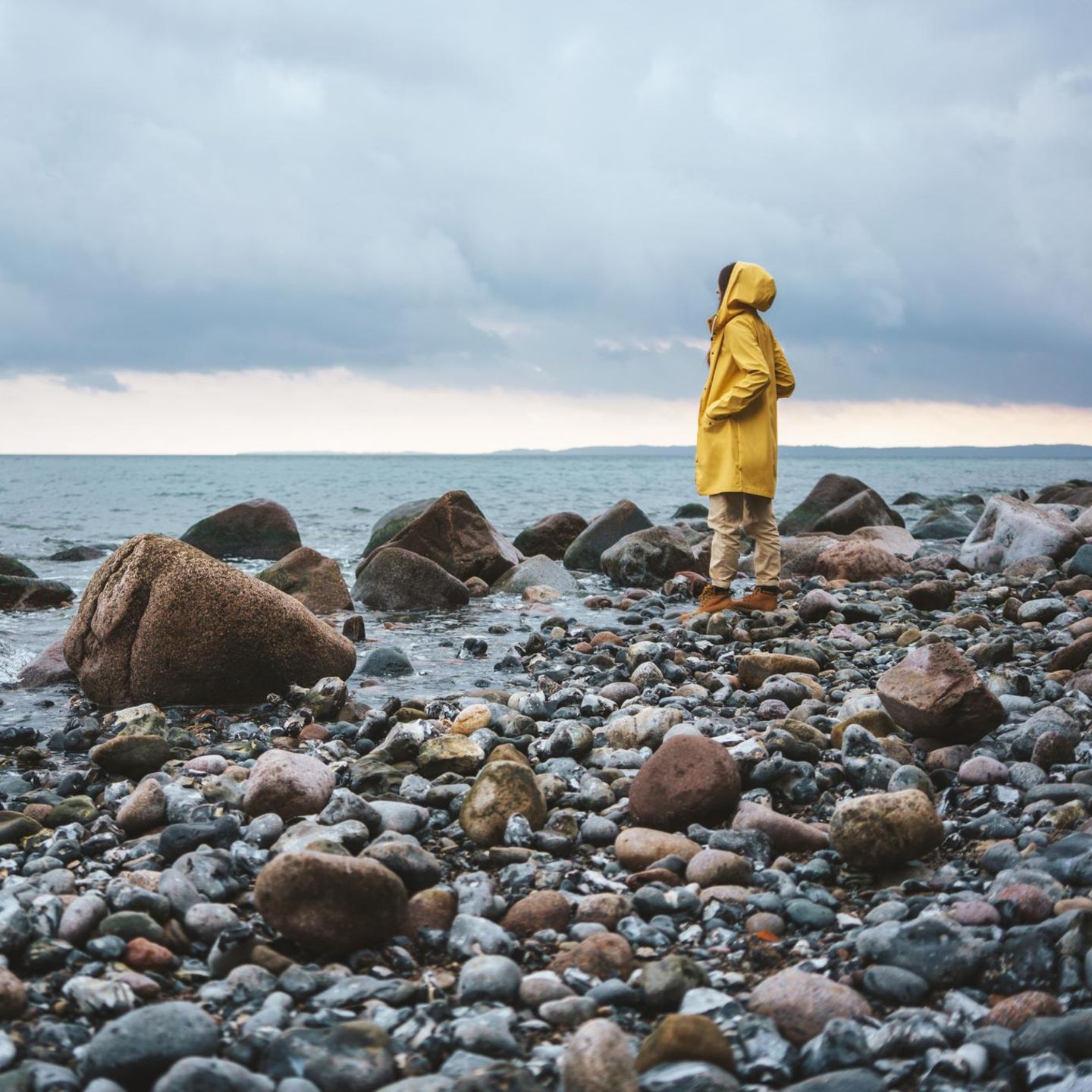 Ein Mensch steht in Regenjacke am Meer und blickt in die Ferne