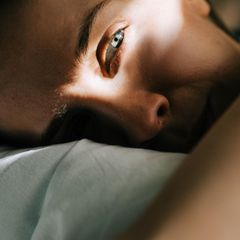 Frau liegt auf dem Bett und schaut aus dem Bild heraus