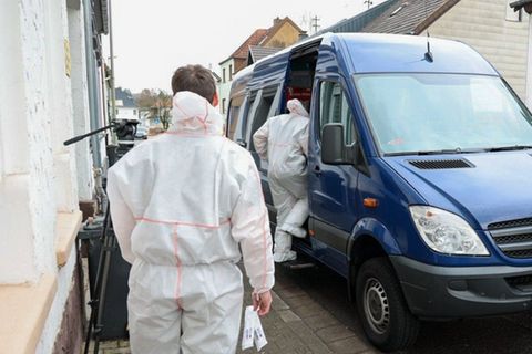 Zwei Mitarbeiter der Spurensicherung besteigen im Saarland in weißen Overalls einen blauen Transporter
