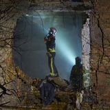 Ein Soldat steht im Einschussloch des Wohngebäudes und wird leicht von Taschenlampenlicht seiner Kollegen beschienen