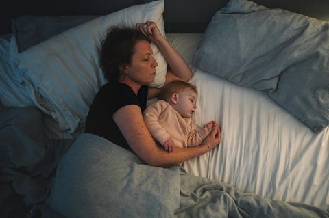 Eine junge Mutter liegt alleine mit ihrem Kind im Bett. Partnerschaft