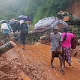 Überlebende eines Erdrutsches überqueren einen Straßenabschnitt, der durch Trümmer blockiert ist