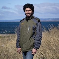 Adrián Simancas, 24, in Punta Arenas in Chile. Er steht in olivgrüner Jacke am Meer