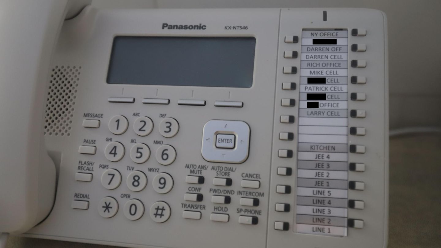 Nahaufnahme eines Festnetztelefons in dem Anwesen. Einige Namen sind geschwärzt. Auf den Kurzwahltasten stehen die Namen Darren, Rich, Mike, Patrick und Larry