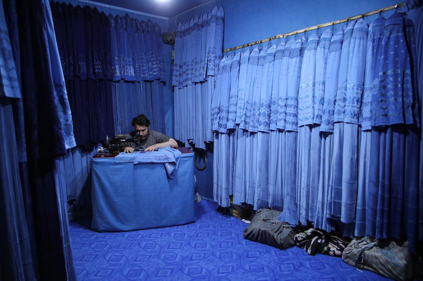 Ein Schneider näht blaue Burkas