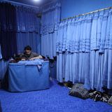 Ein Schneider näht blaue Burkas