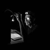 Eine Person sitzt im Dunklen vor einem Computer und richtet die Schreibtischlampe aus, um besser sehen zu können