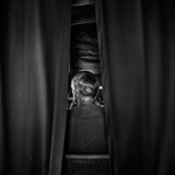 Eine Person von hinten, die zwischen Vorhängen sitzt