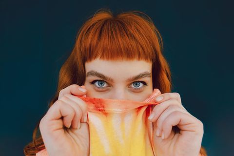 Eine junge Frau versteckt ihre untere Gesichtshälfte in ihrem T-shirt und schaut in die Kamera