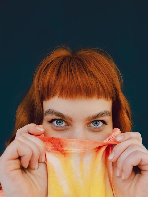 Eine junge Frau versteckt ihre untere Gesichtshälfte in ihrem T-shirt und schaut in die Kamera