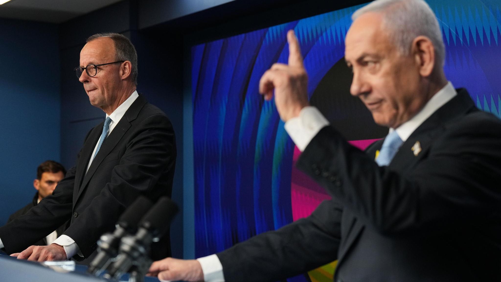 Friedrich Merz und Benjamin Netanjahu stehen nebeneinander hinter Rednerpulten. Netanjahu erhebt den linken Zeigefinger