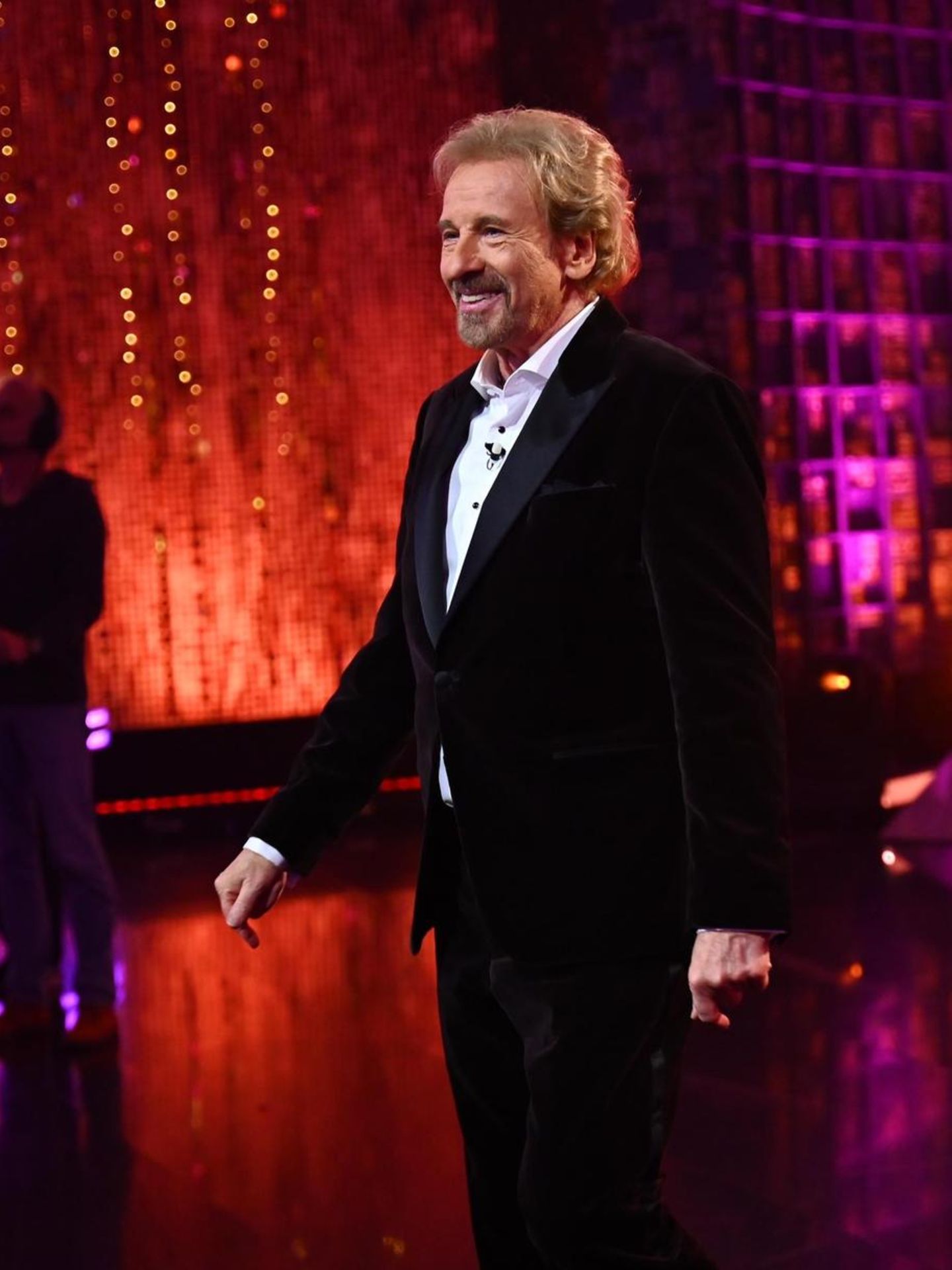 Thomas Gottschalk steht in einem dunklen Anzug mit hellem Hemd im Studio und lächelt