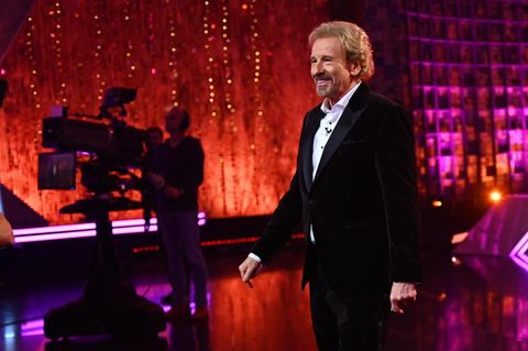 Thomas Gottschalk steht in einem dunklen Anzug mit hellem Hemd im Studio und lächelt