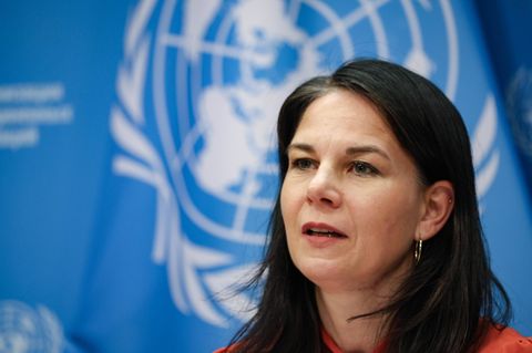 Annalena Baerbock sitzt an einem Tisch und spricht – hinter ihr die hellblau-weiße Flagge der UN