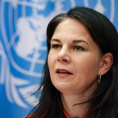 Annalena Baerbock sitzt an einem Tisch und spricht – hinter ihr die hellblau-weiße Flagge der UN