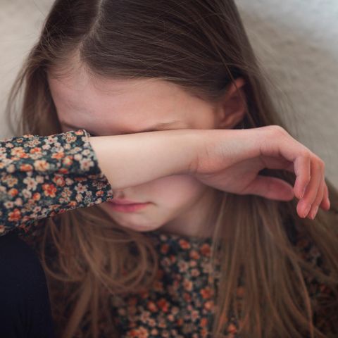 Ein Mädchen verbirgt seine Augen hinter ihrem rechten Unterarm