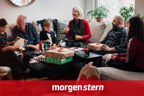 Mehrer Generationen sitzen Weihnachten auf einem Ecksofa, während Kinder Geschenke auspacken
