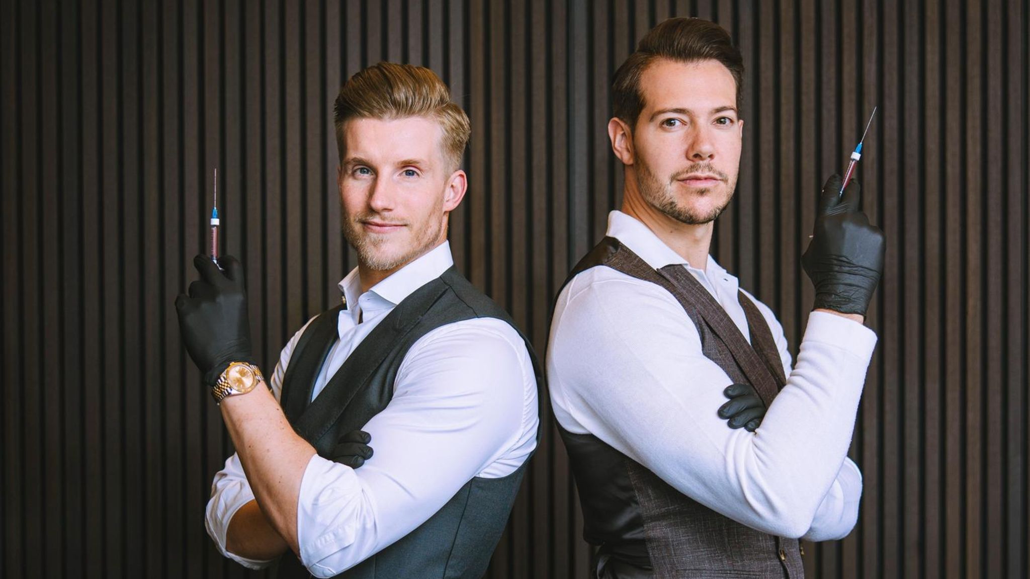 Dr. Rick und Dr. Nick: zwei Männer in Anzügen und Gummihandschuhen halten Spritzen in der Hand