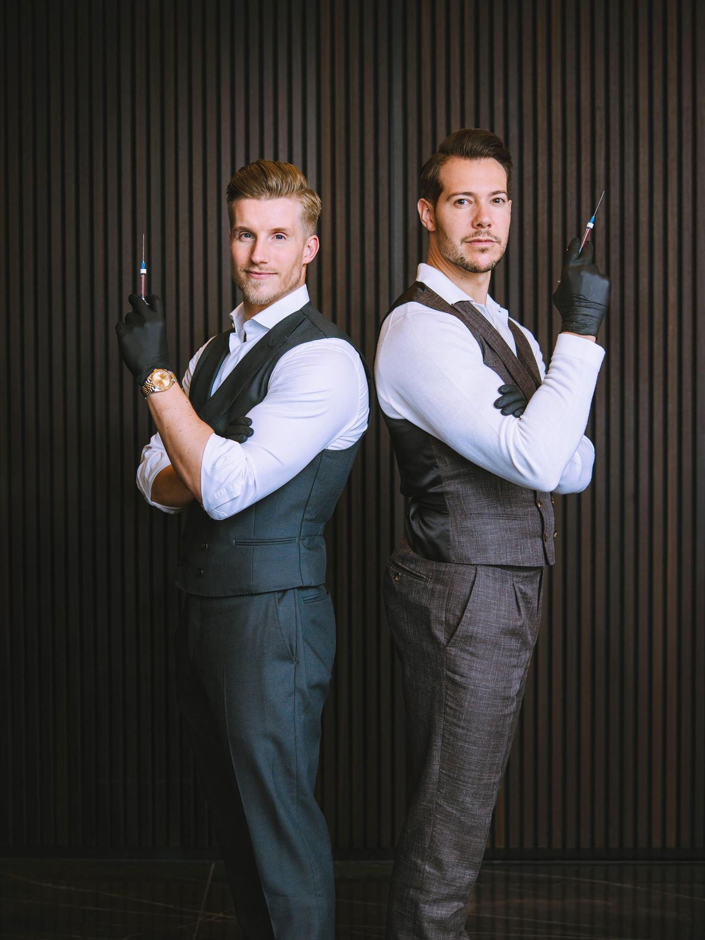 Dr. Rick und Dr. Nick: zwei Männer in Anzügen und Gummihandschuhen halten Spritzen in der Hand