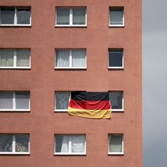 Die Bundesflagge hängt zwischen zwei Fenstern eines Plattenbaus in Halle/Saale. (Archivbild) Foto: Hendrik Schmidt/dpa