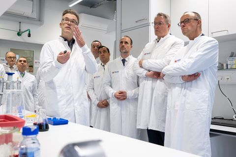 Kanzler Merz, Ministerpräsident Schweitzer und der rheinland-pfälzische Wissenschaftsminister Hoch bekommen ein Projekt erklärt,