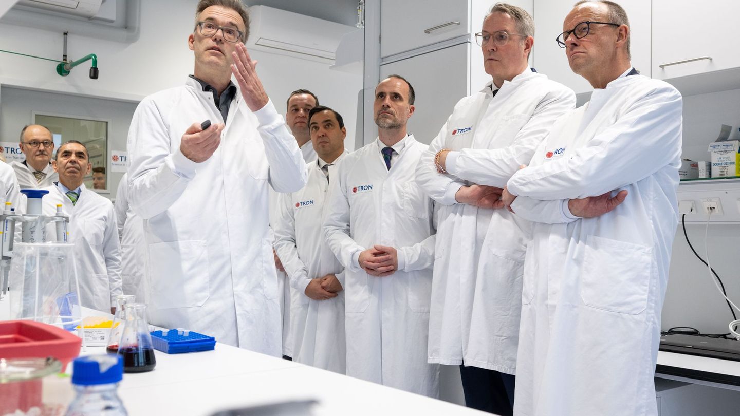 Kanzler Merz, Ministerpräsident Schweitzer und der rheinland-pfälzische Wissenschaftsminister Hoch bekommen ein Projekt erklärt,