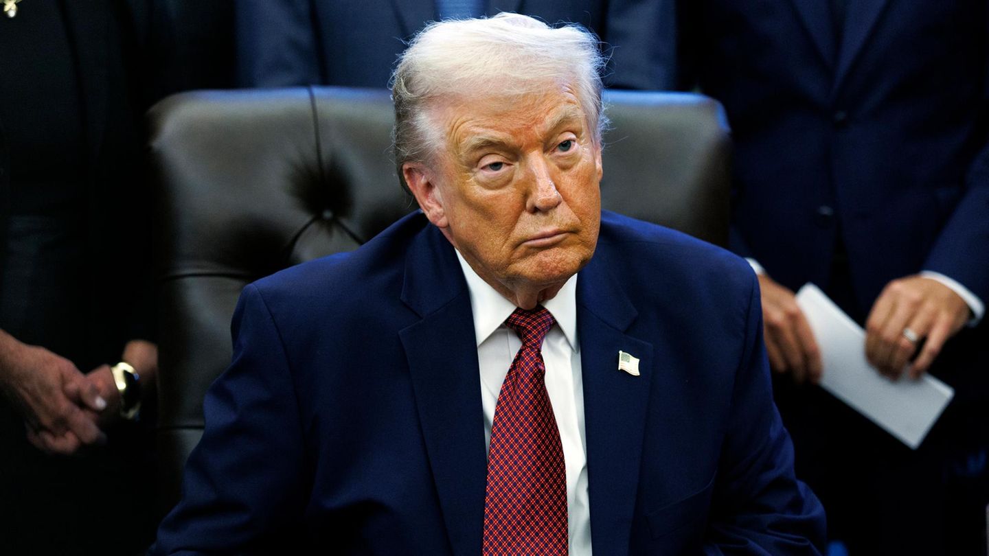 Donald Trump sitzt an einem Tisch und schaut mit zusammengekniffenen Lippen nach vorne