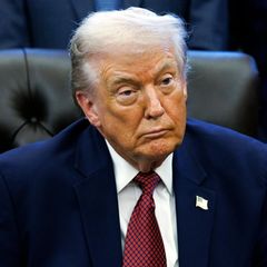 Donald Trump sitzt an einem Tisch und schaut mit zusammengekniffenen Lippen nach vorne