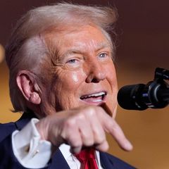 Donald Trump zeigt mit seinem rechten Zeigefinder nach unten, während er bei einer Rede in ein Mikrofon spricht