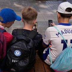 Kinder in Australien benutzen ihre Telefone, während sie vor einer Schule in Sydney sitzen