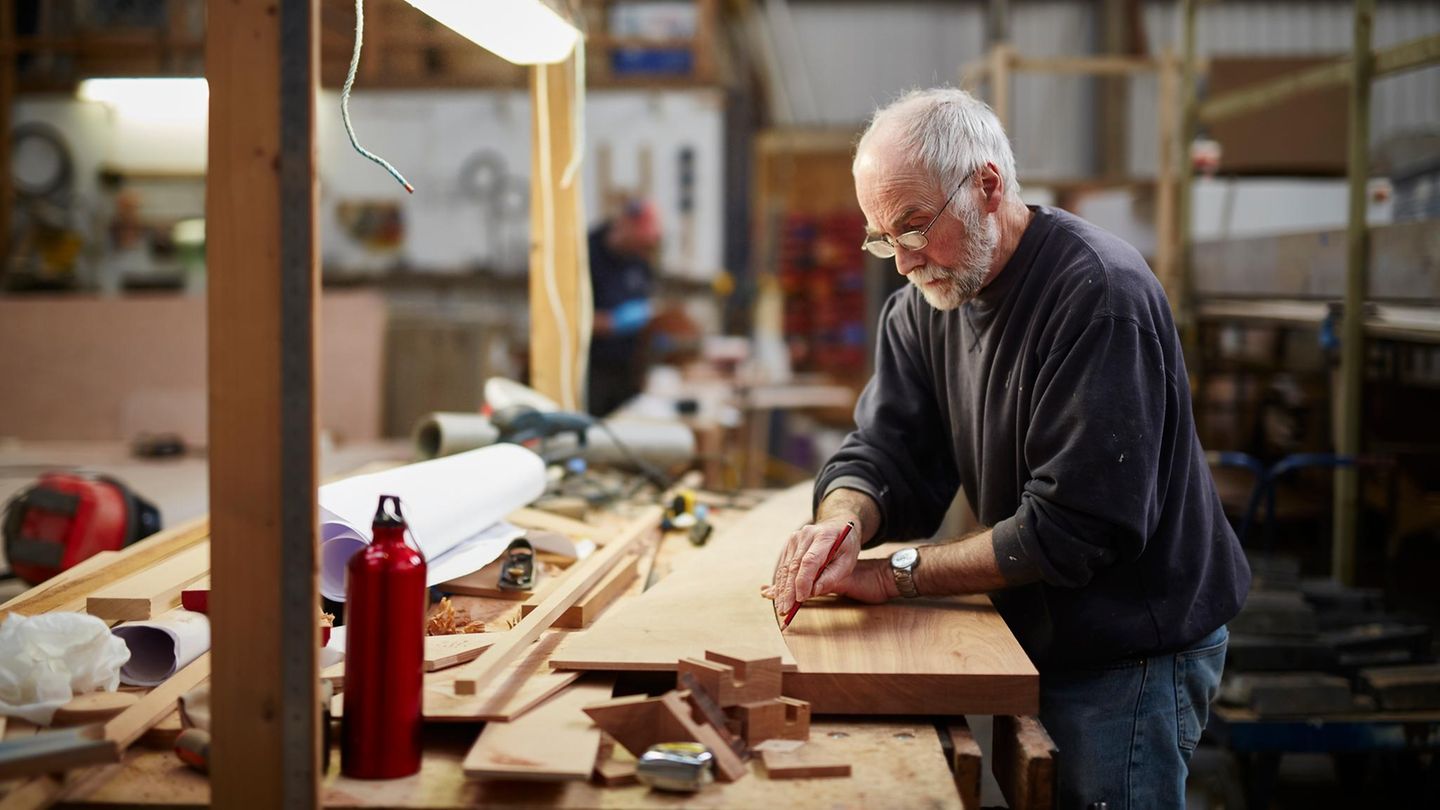 Handwerker in fortgeschrittenem Alter bereitet eine Holzplatte fürs Zuschneiden vor: Rente mit 70 Symbolbild