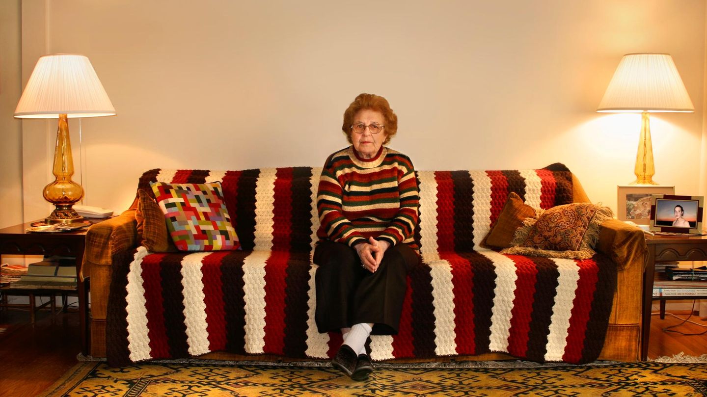 Rente ohne gearbeitet zu haben, Symbolbild: Ältere Frau sitzt auf gemustertem Sofa