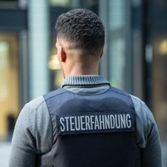 Ein Mann trägt eine Weste mit dem Schriftzug "Steuerfahnder" auf dem Rücken