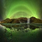 Bögen von grünem Polarlicht über einem Berg mit Wasserfall