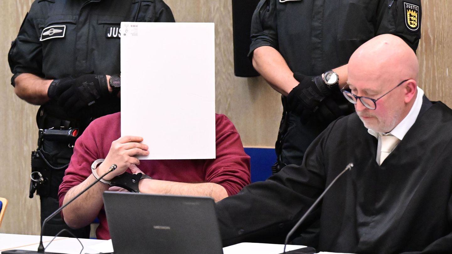 Der Angeklagte in einem Mordprozess nach einer Todesfahrt von Mannheim sitzt mit einem Aktendeckel vor seinem Gesicht im Gericht