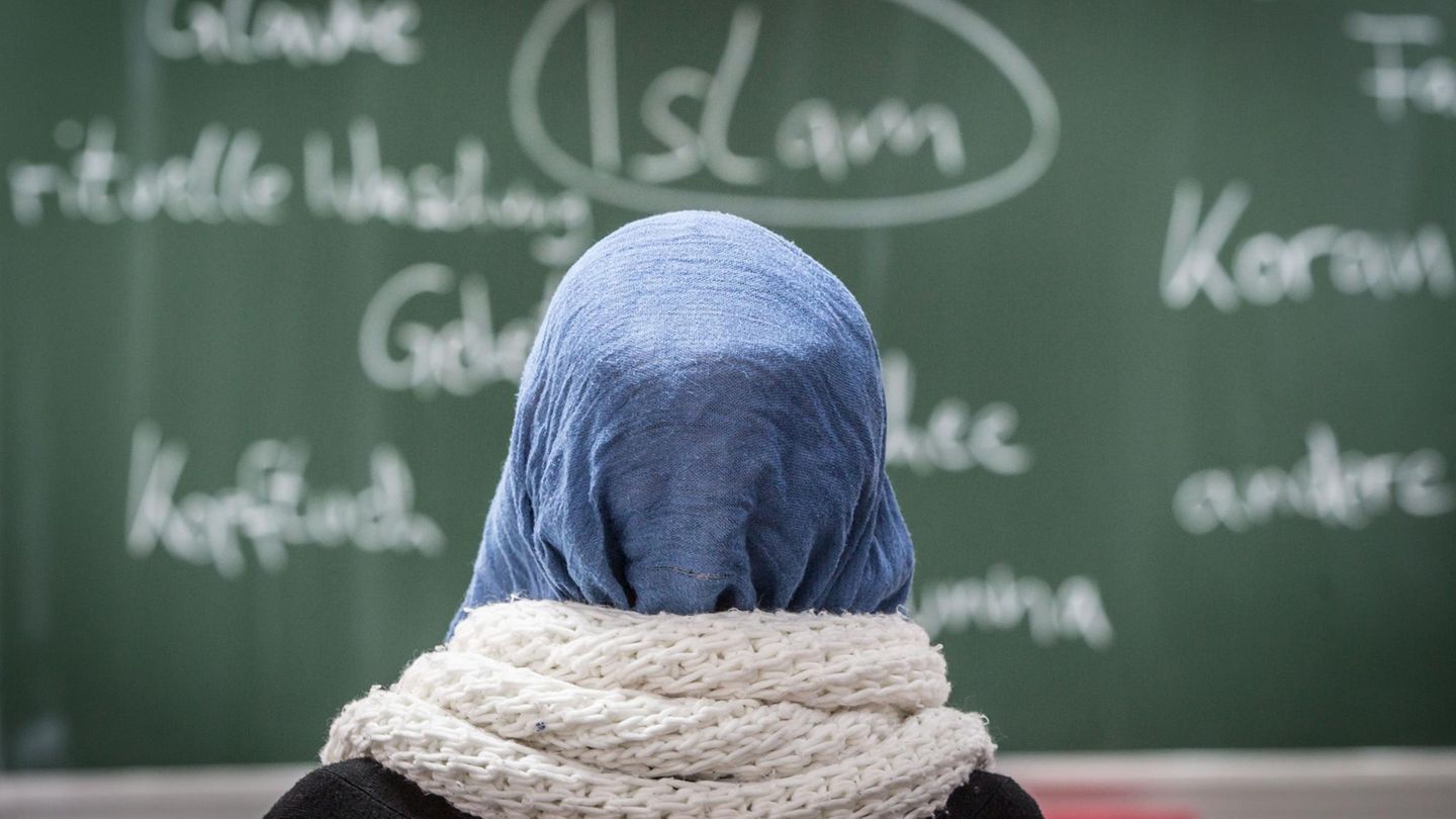 Eine junge Frau mit Kopftuch sitzt in einer Schule vor einer Tafel
